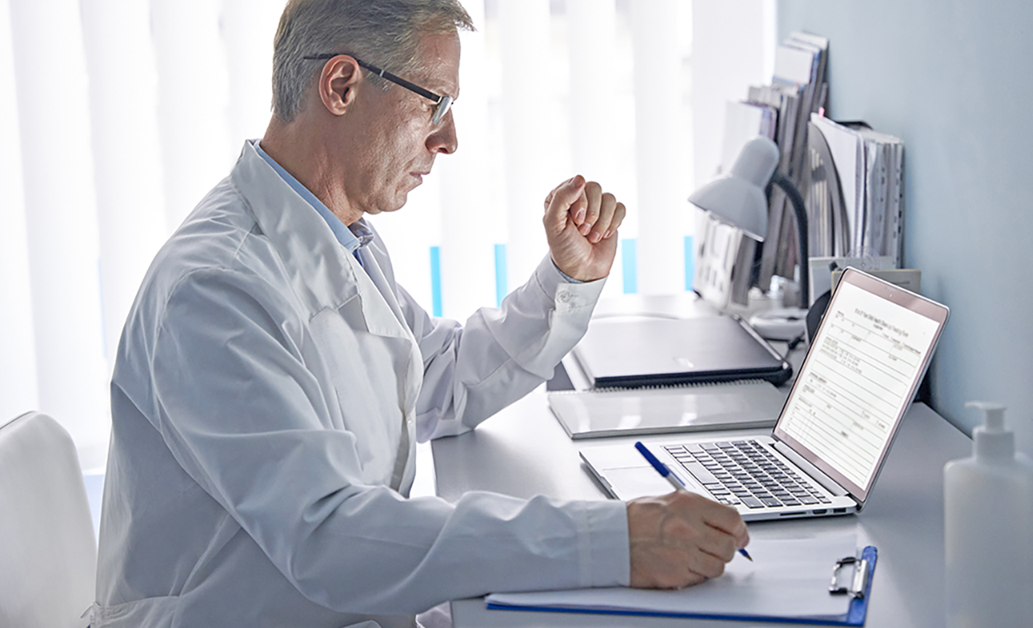 Serious mature old doctor physician using laptop tech in hospital office. Senior middle aged male gp checking patient clinical registration form, elearning working looking at computer sitting at desk.