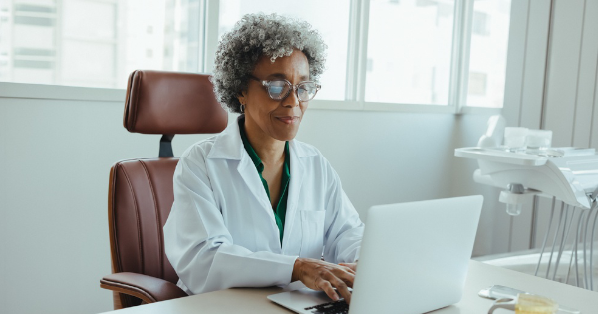 A dentist sits in her office looking at her computer.