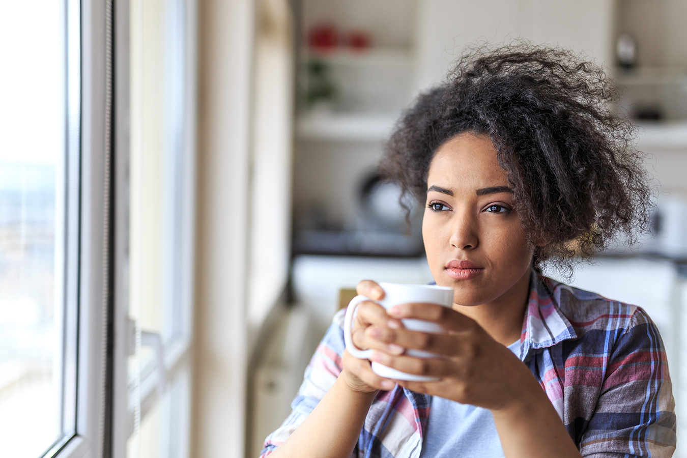 Sad african woman drinking coffee at home.