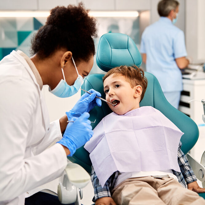Black,Female,Dentist,Examining,Small,Boy's,Teeth,During,Dental,Procedure