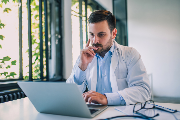 Portrait of a serious doctor using laptop in medical office.