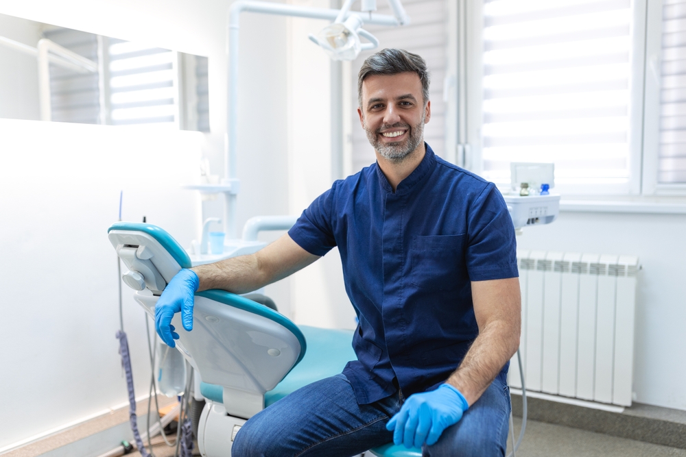 Male,Dentist,Posing,At,Clinic,Over,Modern,Cabinet,,Empty,Space.