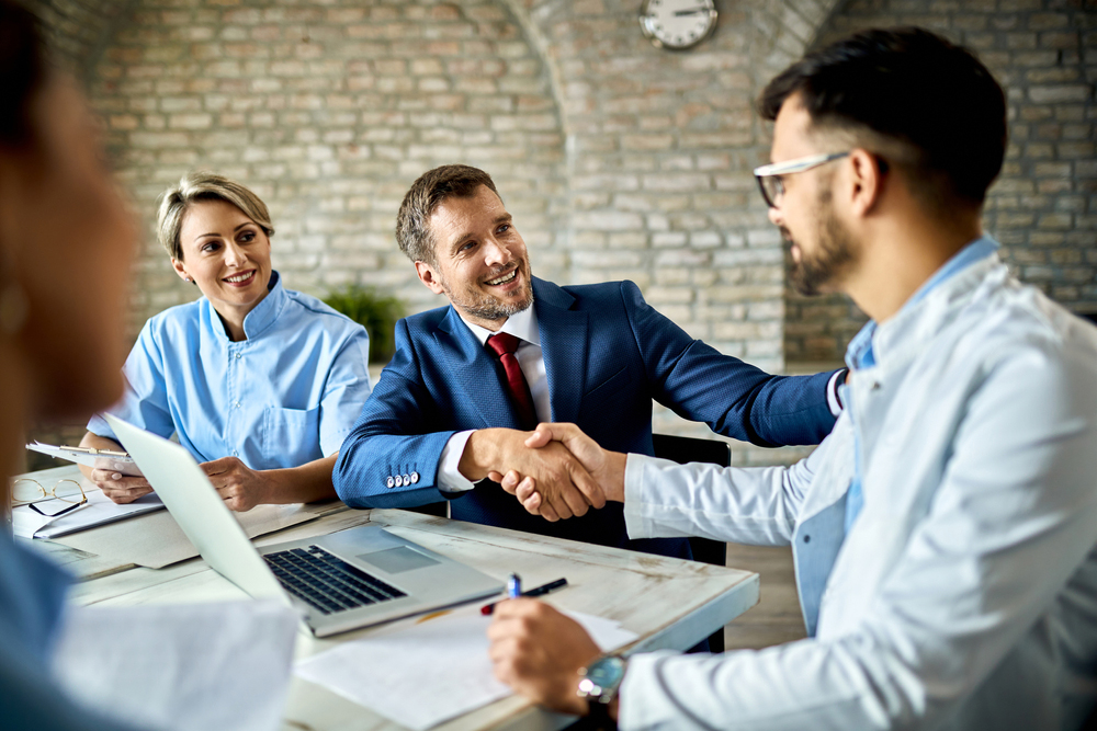 Happy,Financial,Advisor,And,Male,Doctor,Shaking,Hands,After,Successful Happy financial advisor and male doctor shaking hands after successful meeting in the office.
