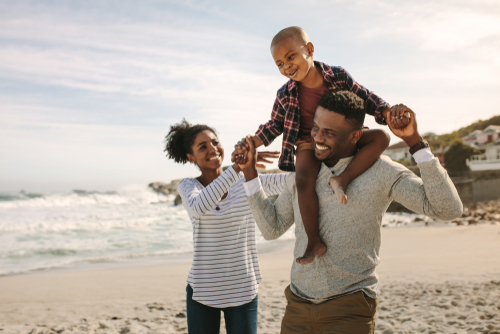 Parents,Carrying,Son,On,Shoulders,On,Beach,Vacation.,African,Family