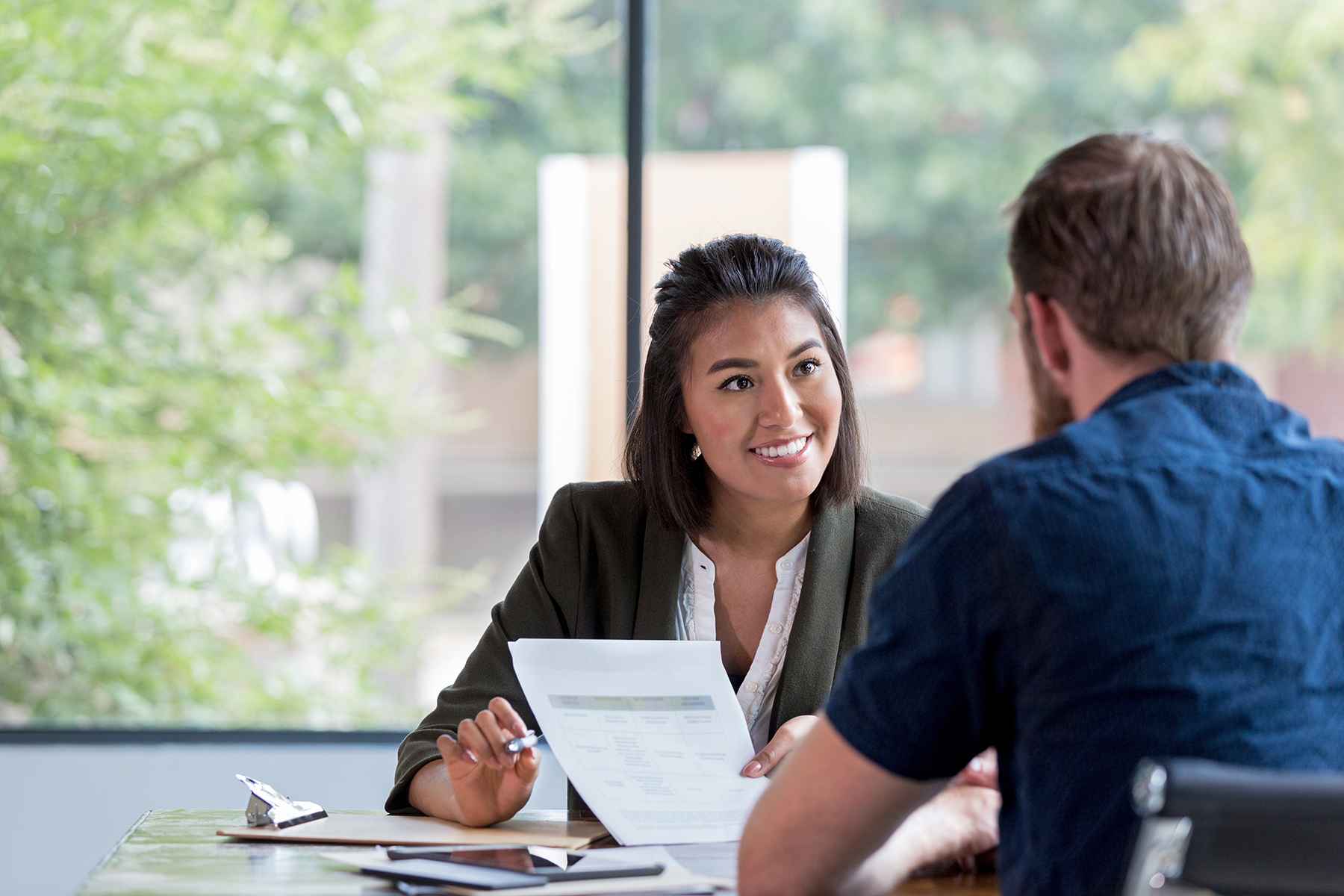 Hispanic businesswoman smiles while showing a document to a male associate.